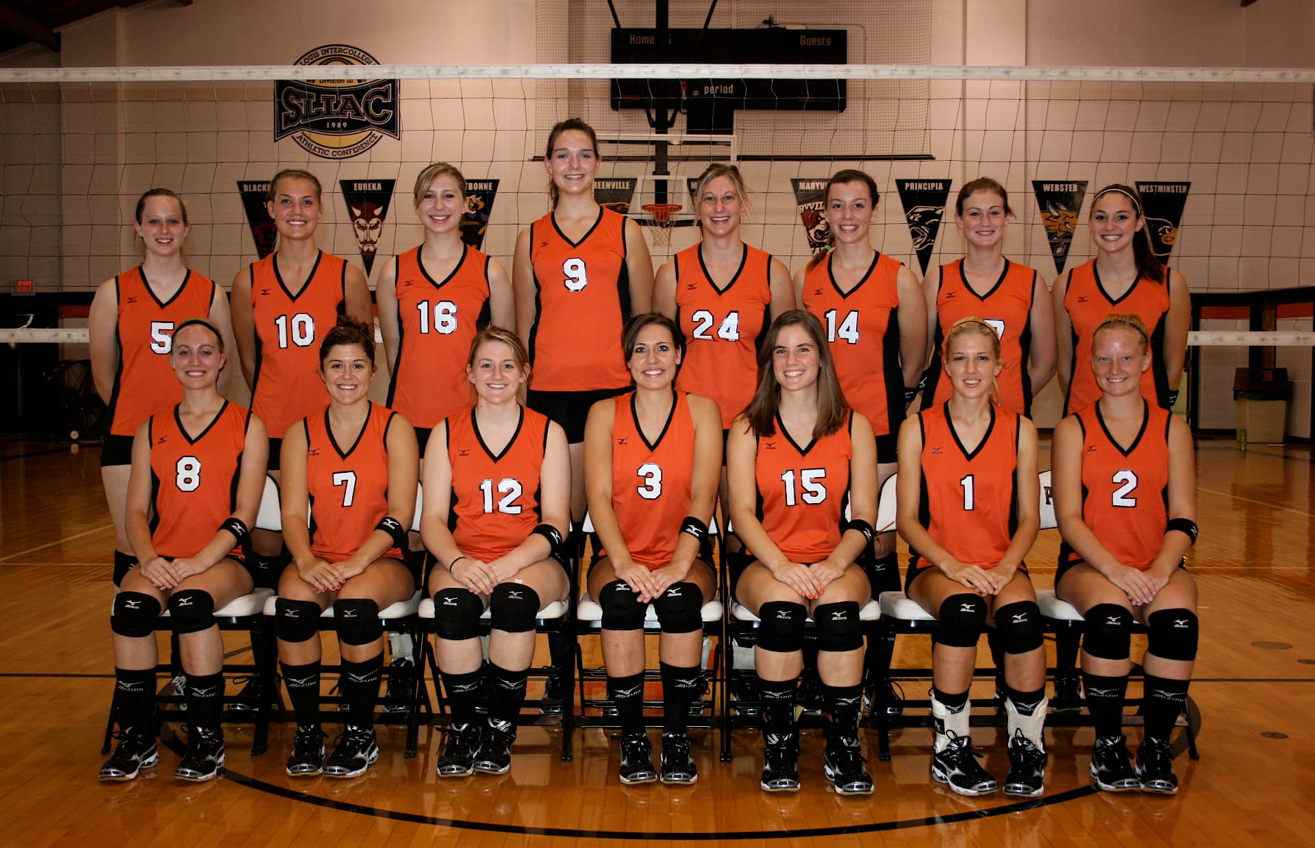 Greenville women's volleyball team photo in orange jerseys with SLIAC banners behind the net.