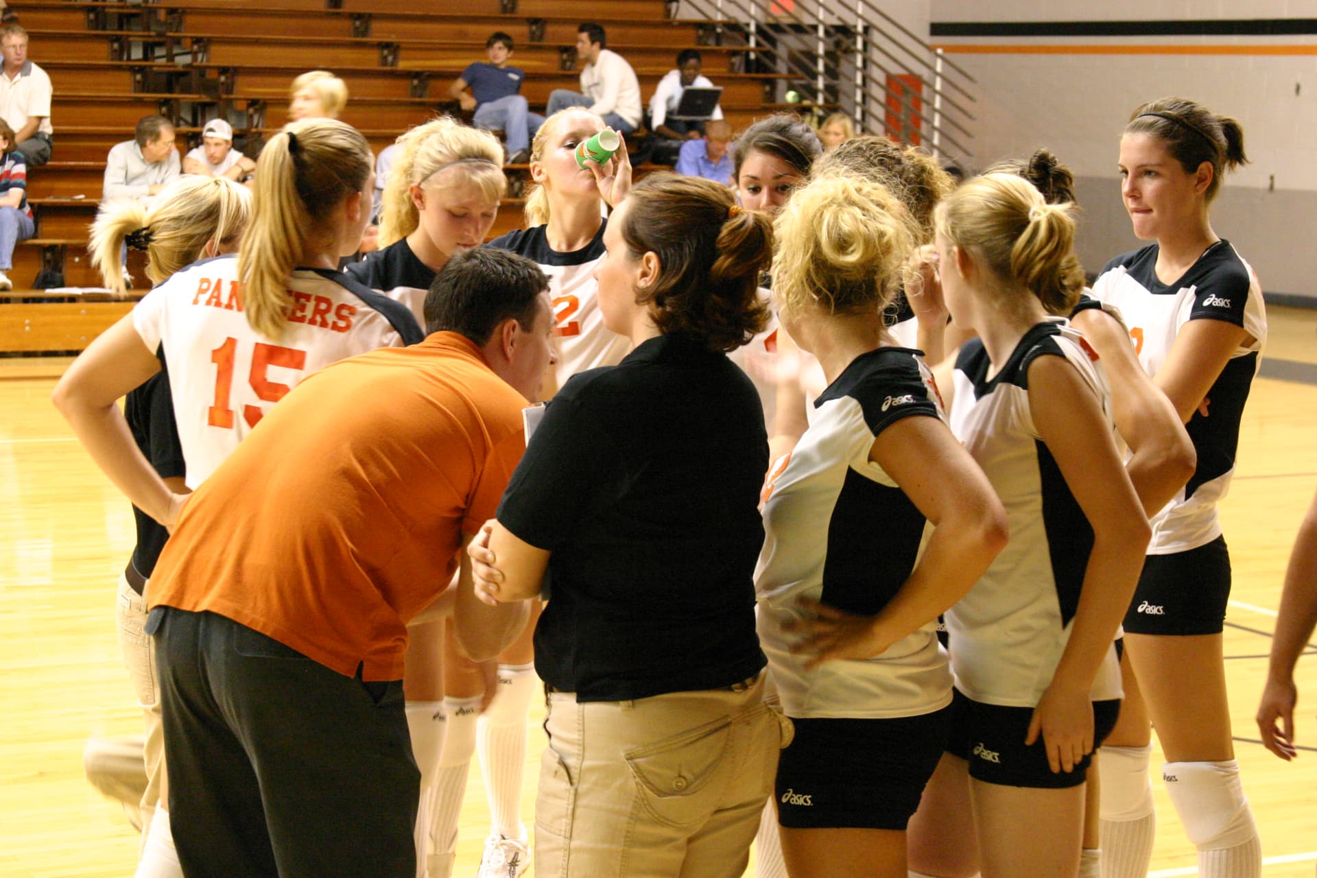 Greenville volleyball coaches talking with players in a courtside huddle during a match.